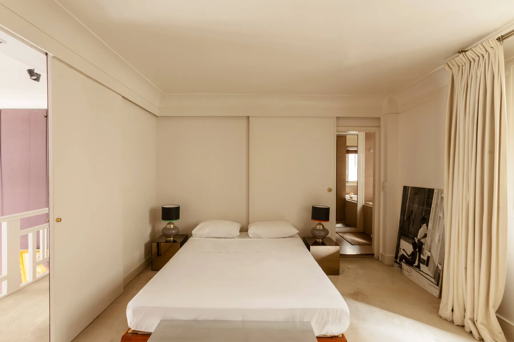 Un dormitorio con una cama blanca, mesitas de noche y cortinas largas.