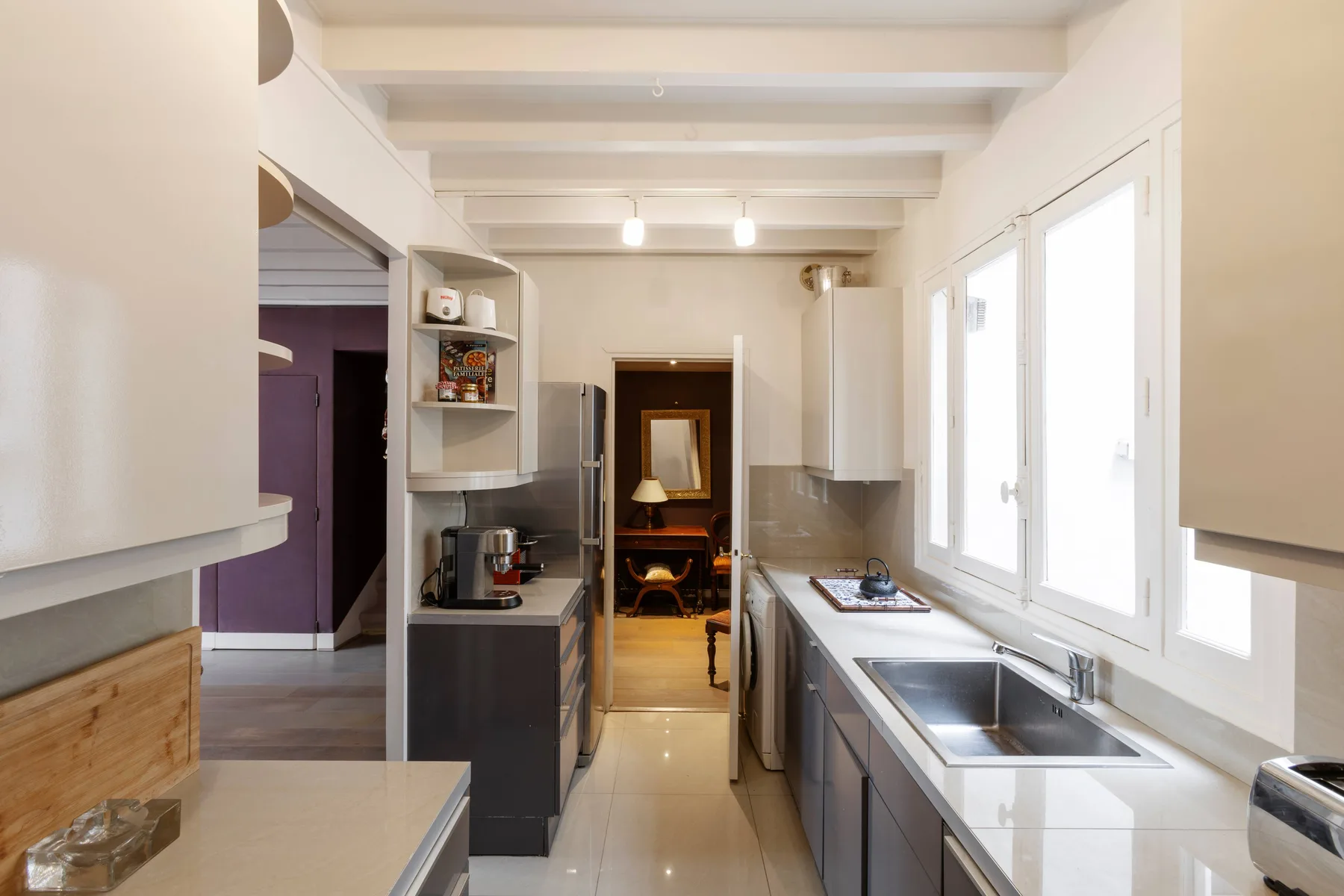 Una cocina estrecha con encimeras, un fregadero y ventanas luminosas a un lado.