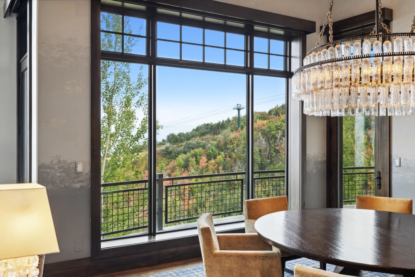 A dining area with a round table beside large windows overlooking greenery.