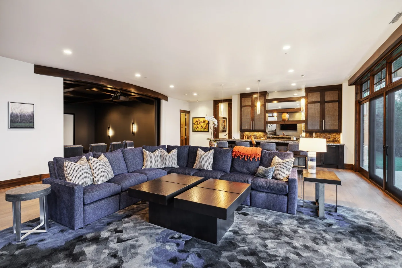 A spacious living room with sectional seating, dark coffee tables, and an open kitchen.