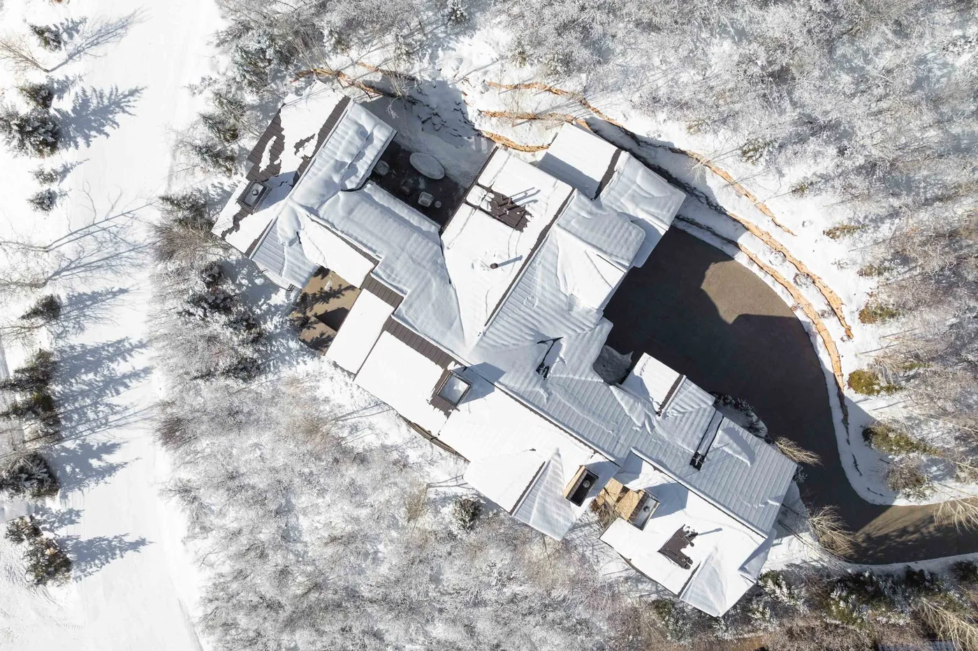 An aerial view of a snow-covered house surrounded by trees.