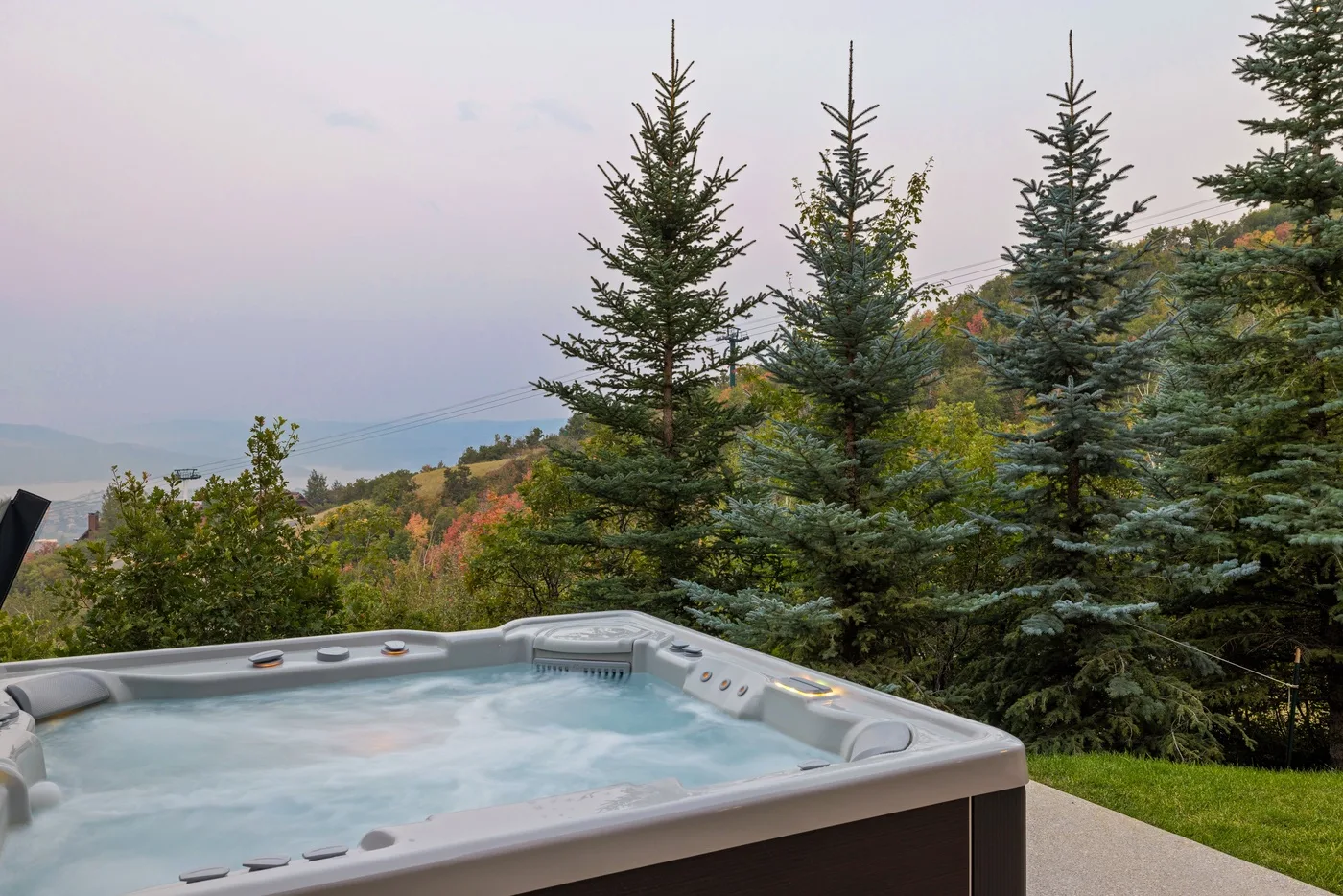 An outdoor hot tub overlooks evergreen trees and a wooded hillside.