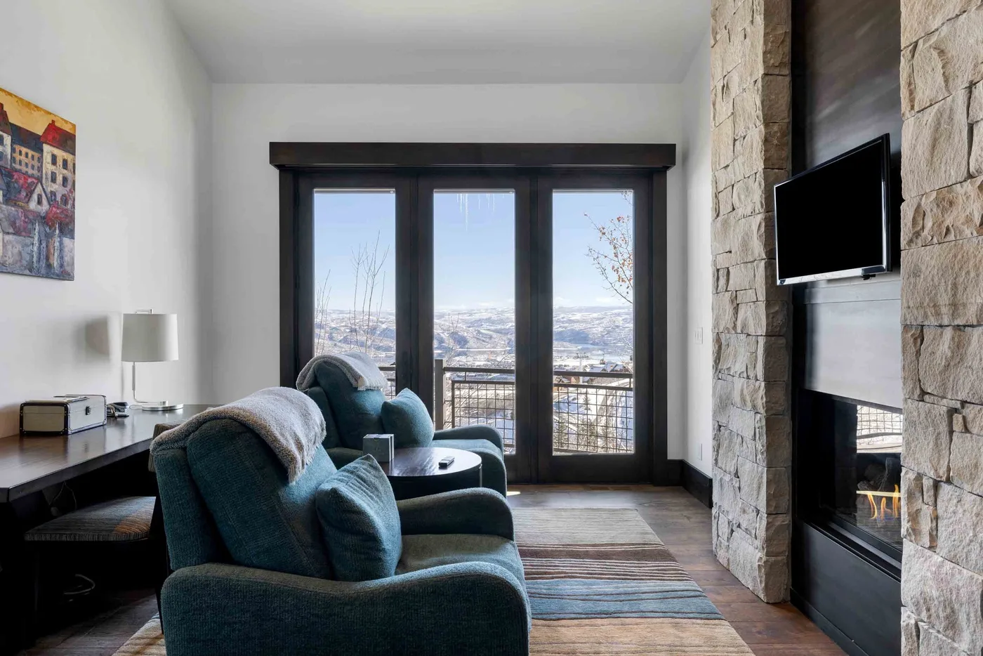 A living room with seating, a stone fireplace, and large windows overlooking the landscape.