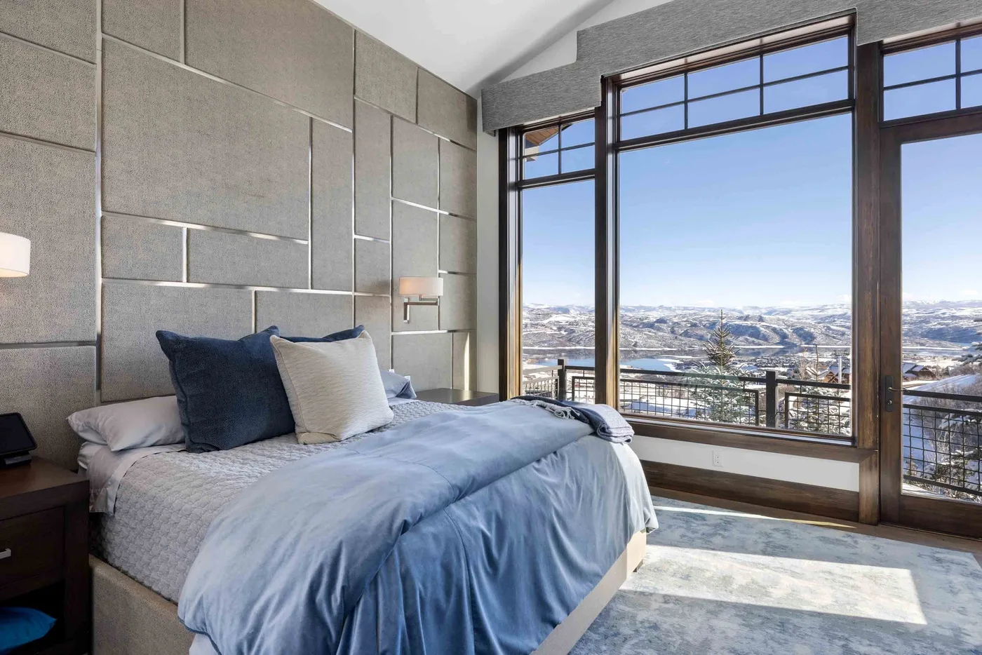 A bedroom with a bed beside large windows overlooking a snowy landscape.