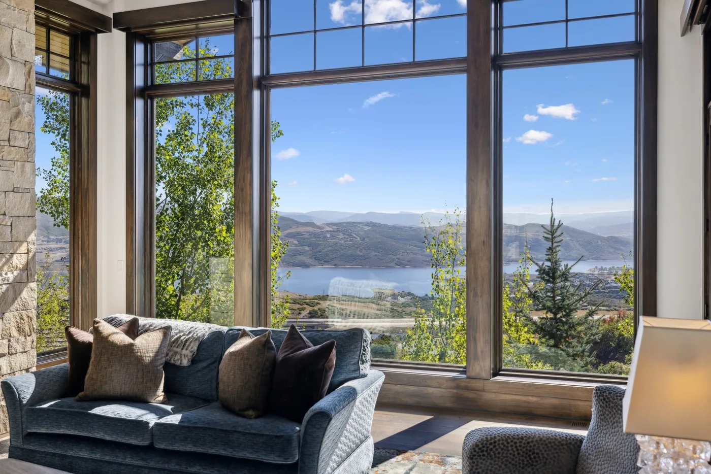 A living room with seating beside large windows overlooking a lake and hills.