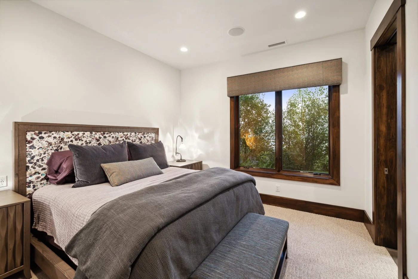 A bedroom with a large bed and a window overlooking leafy trees.