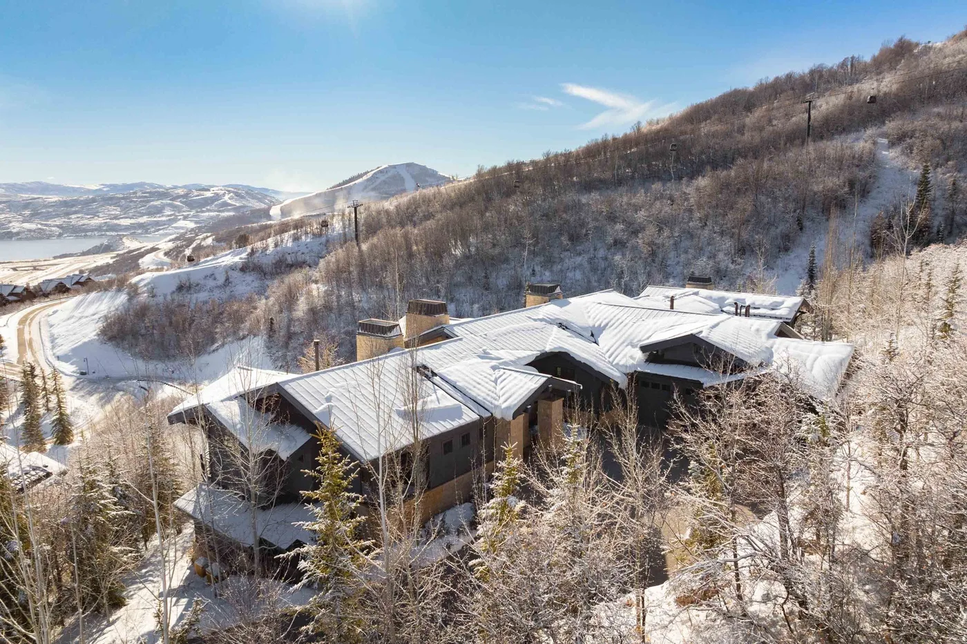 Snow-covered buildings sit among frosted trees on a wooded hillside beneath a clear sky.