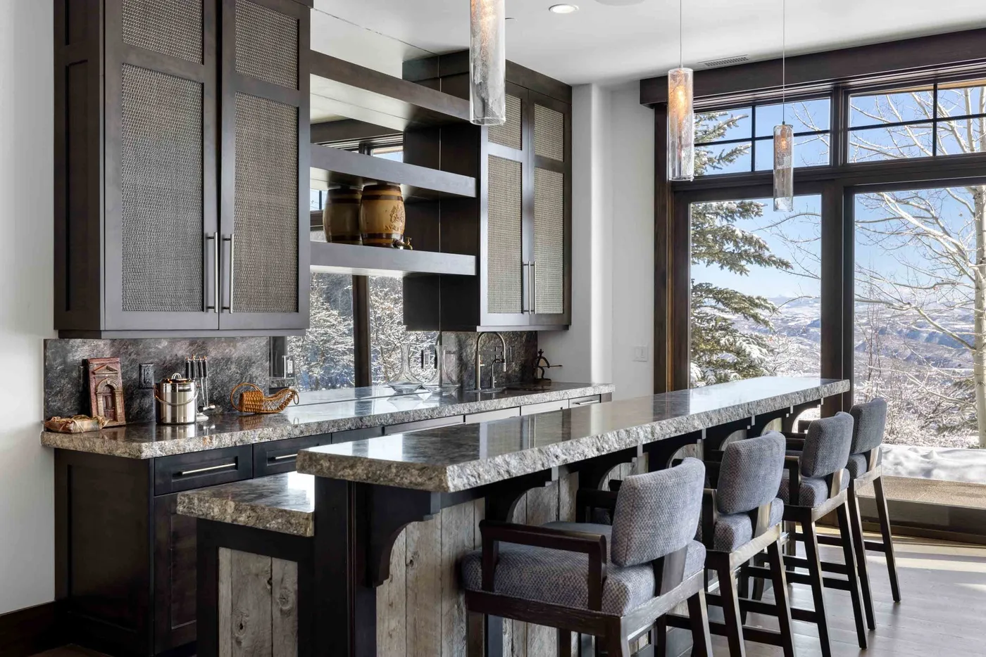 A modern kitchen with a long island and seating beside large windows.