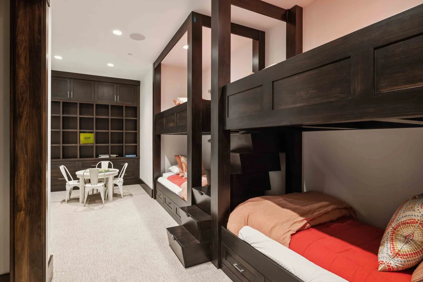 A bedroom with dark bunk beds and a small dining table beside built-in shelving.