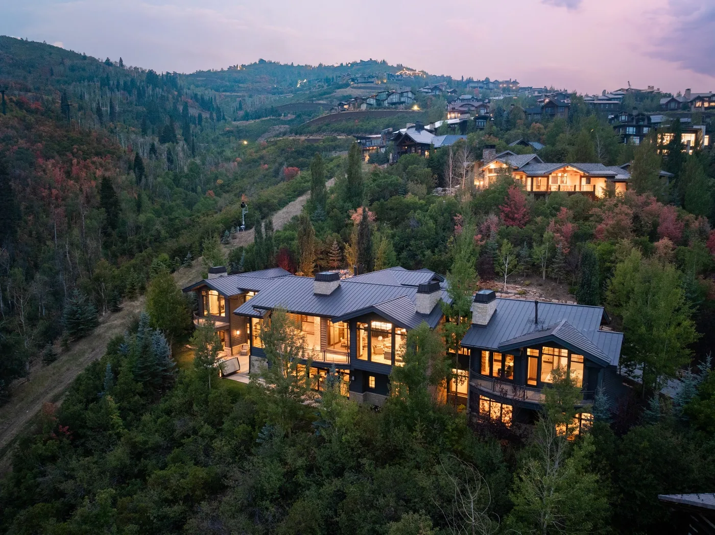 Aerial view of illuminated houses scattered across a wooded hillside at dusk.