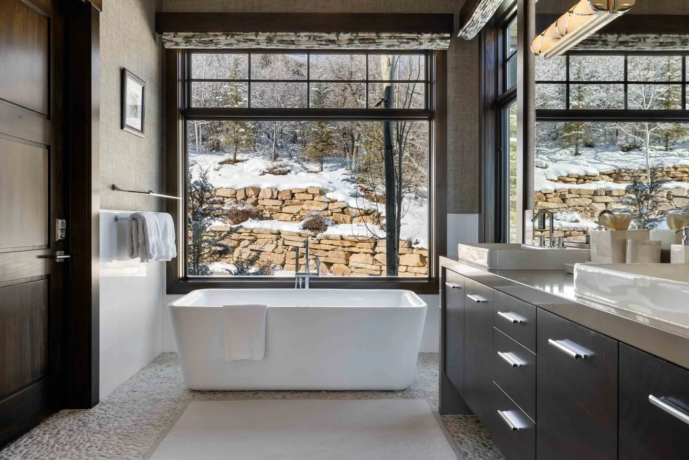 A bathroom with a freestanding bathtub beneath large windows overlooking a snowy landscape.