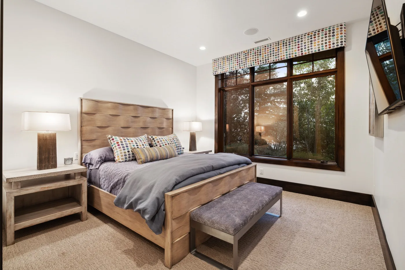 A bedroom with a wooden bed, gray bedding, and a large window.