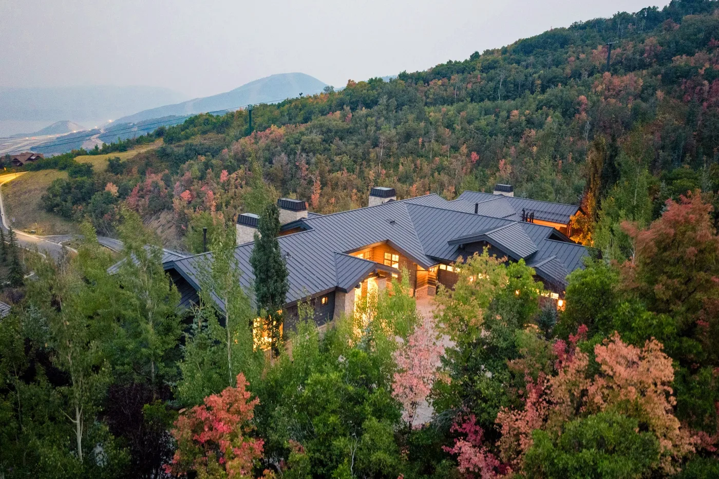 A large building sits among wooded hills with autumn-colored trees.