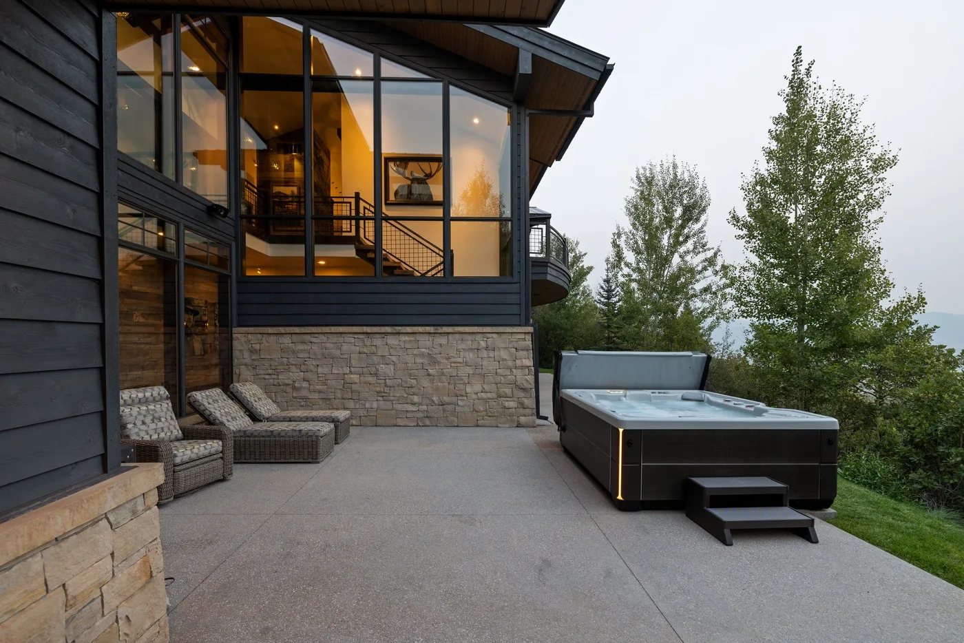 A modern house patio with a hot tub beside large windows and trees.