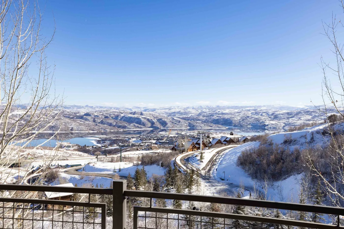 A snowy mountain valley and lake are visible from a fenced overlook.
