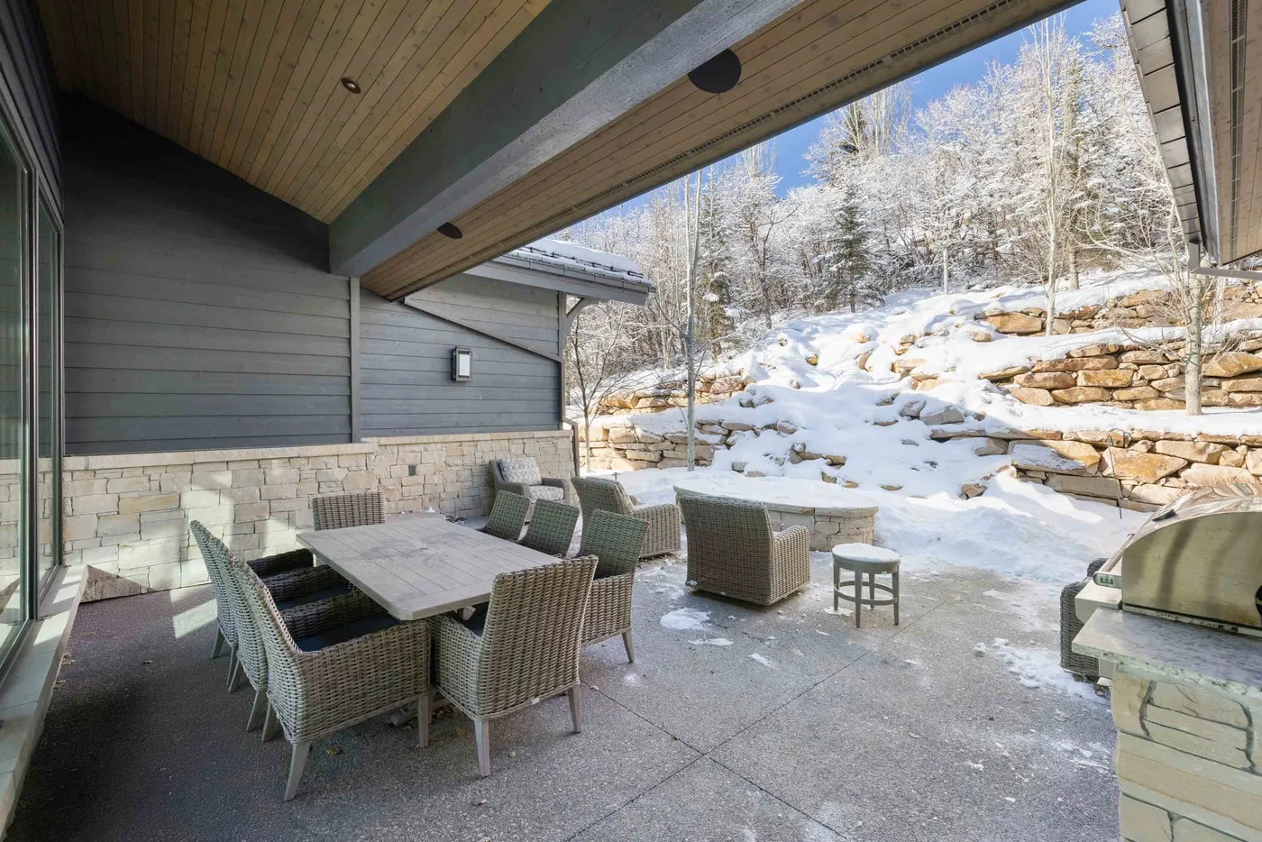A covered patio with outdoor seating overlooks a snow-covered, wooded slope.