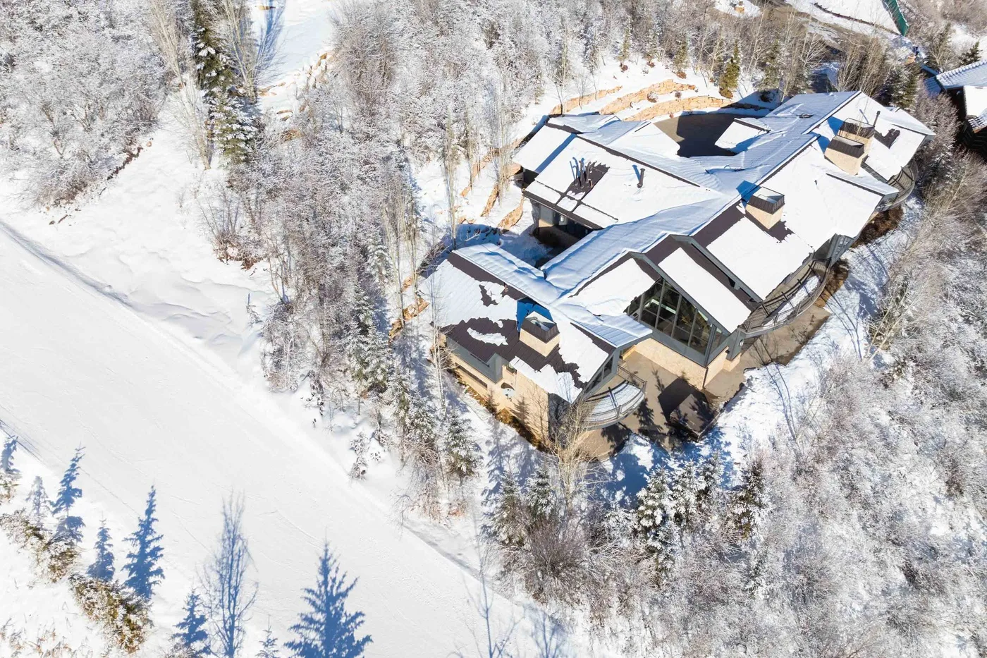 An aerial view of a large building with snow-covered roofs among snowy trees.