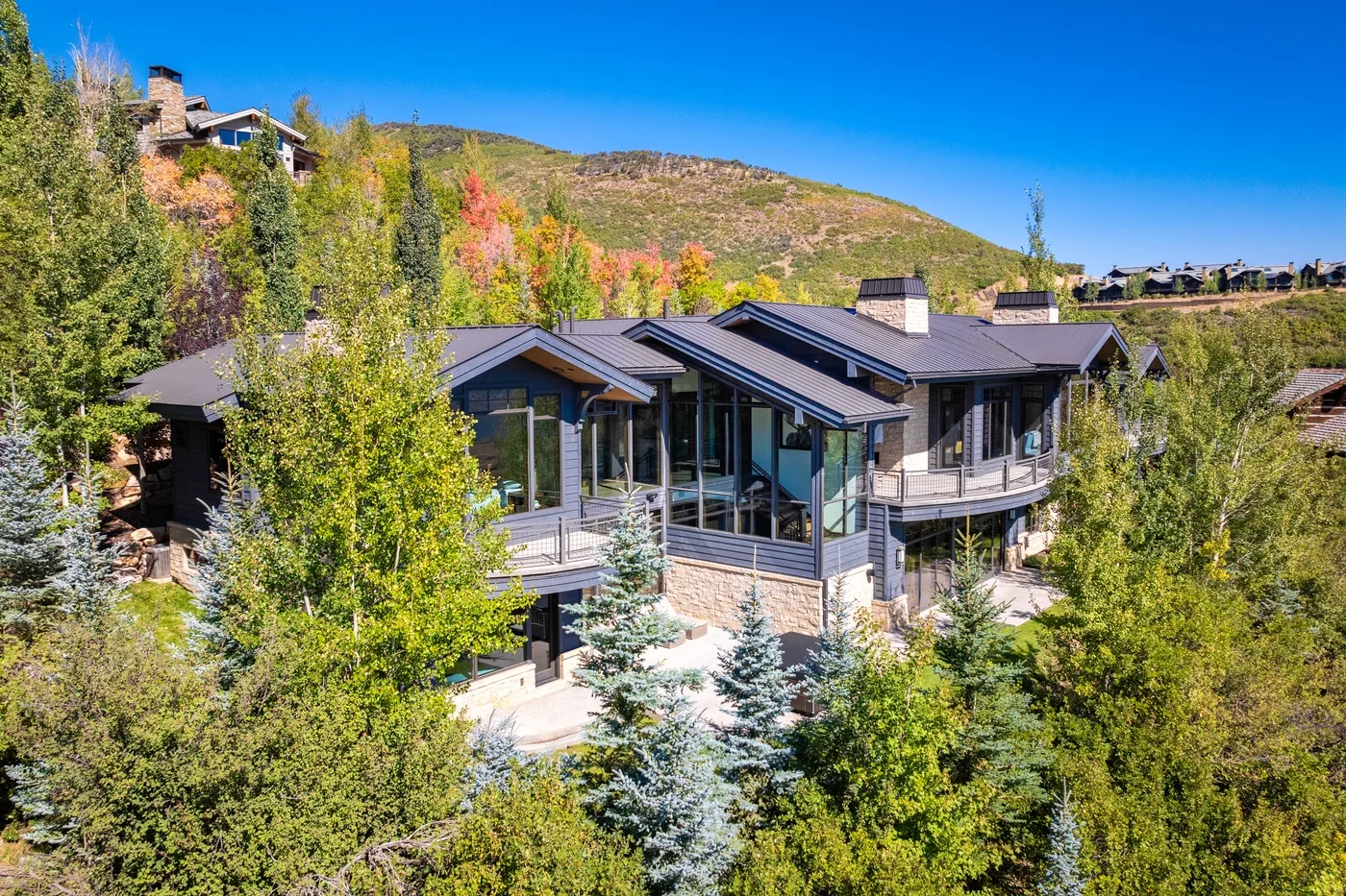 A modern house sits among trees on a hillside beneath a clear blue sky.