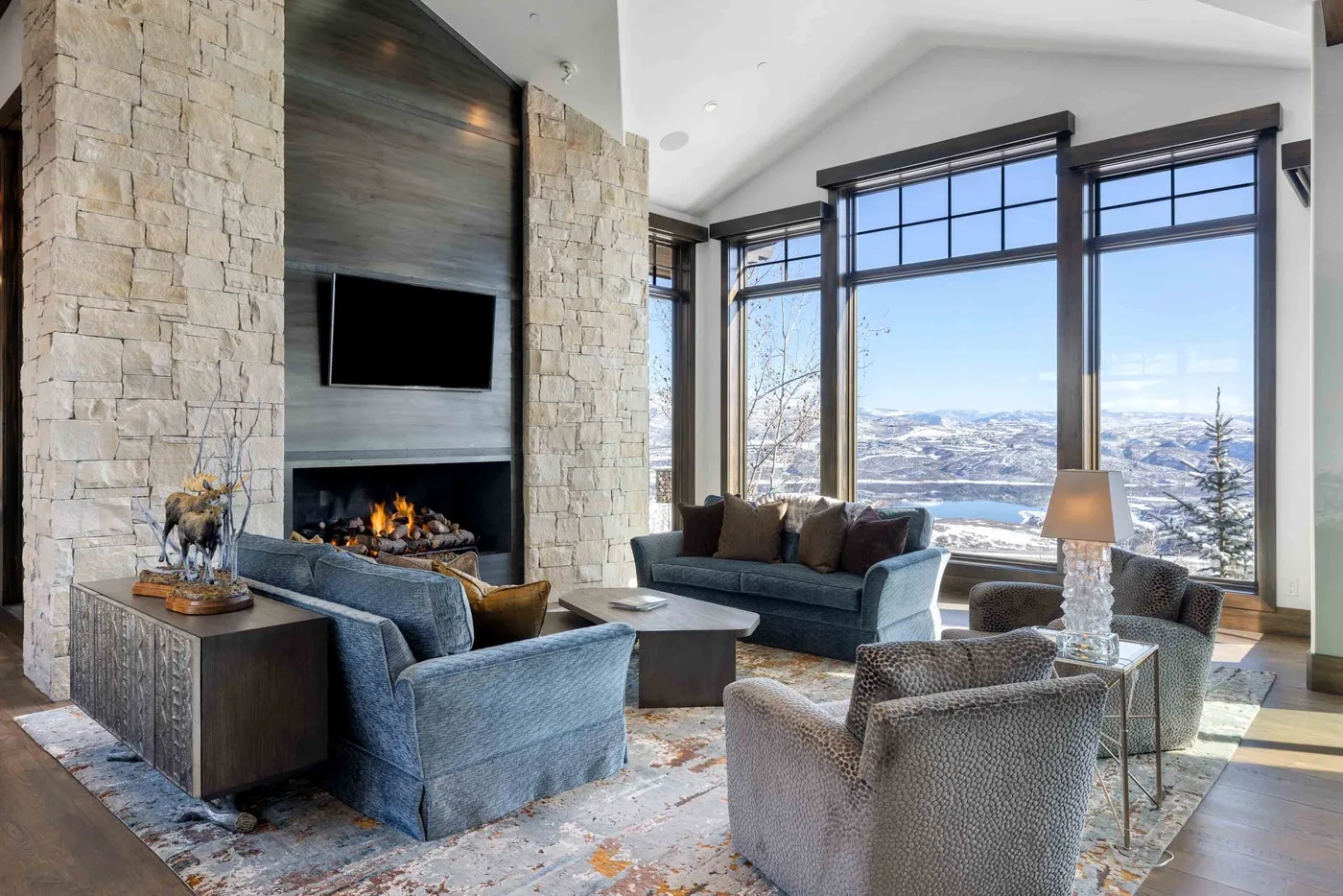 A living room with seating arranged around a fireplace and large windows.