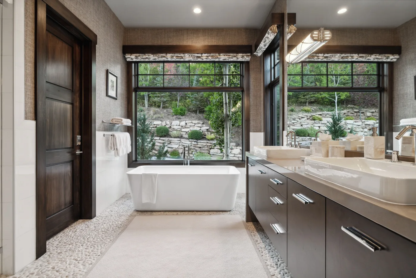 A bathroom with a freestanding tub beneath large windows overlooking a garden.