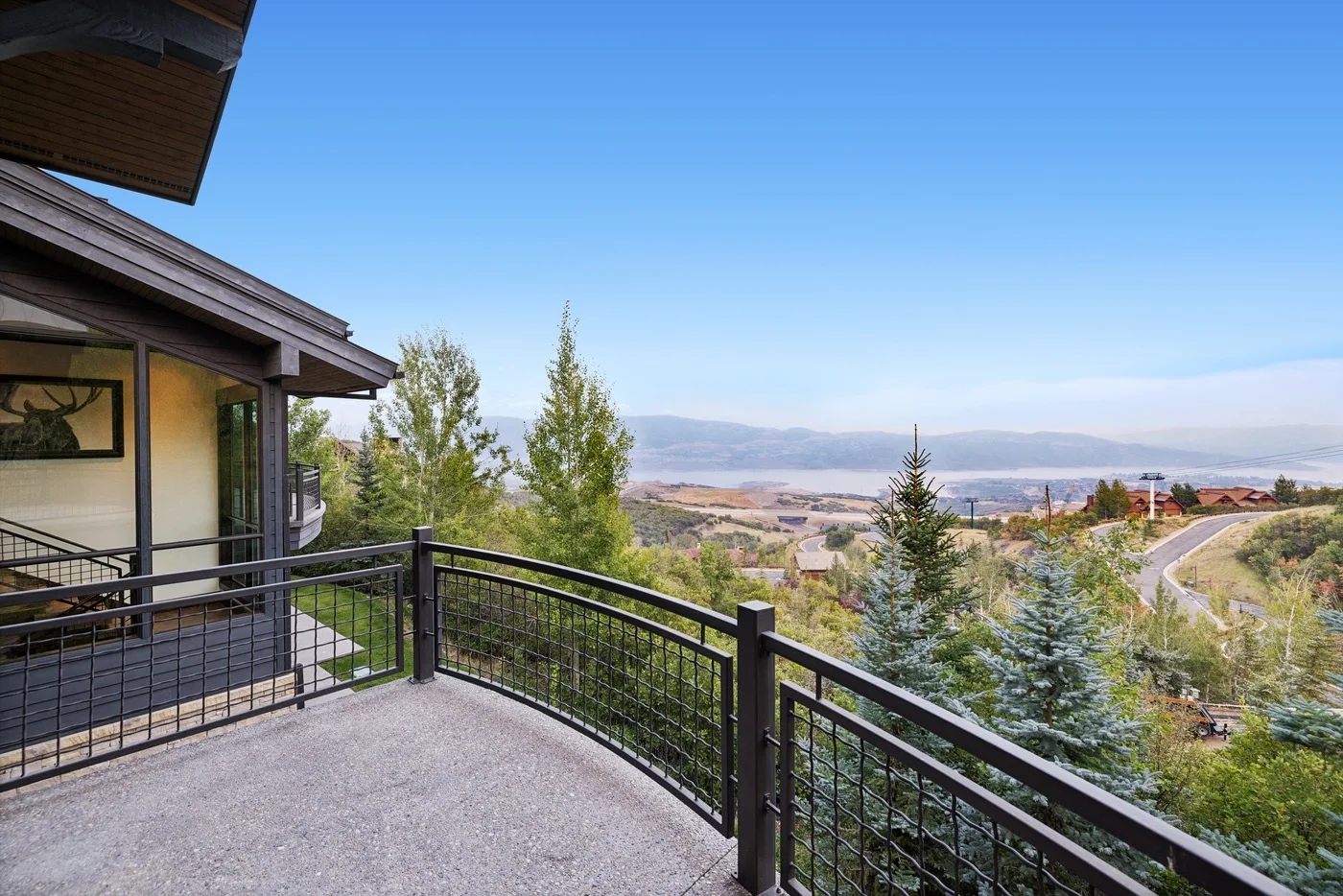 A terrace with metal railings overlooks trees, a road, and a distant landscape.