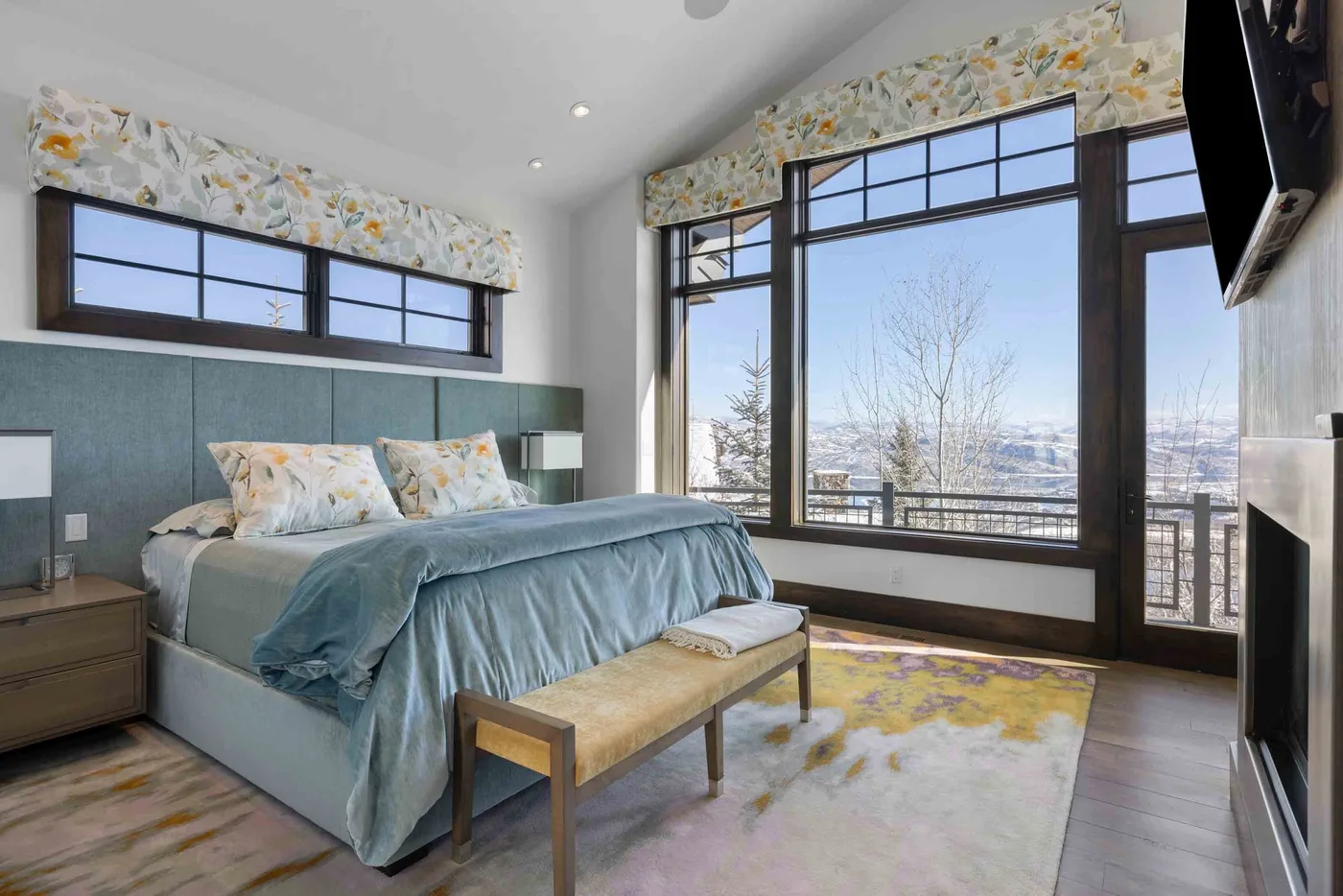 A bedroom with a bed beside large windows overlooking a snowy landscape.