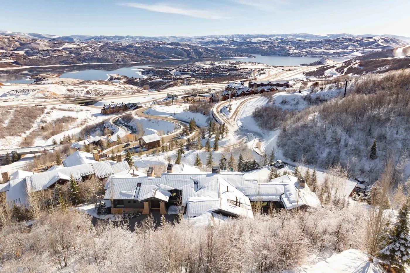 Snow-covered homes sit among wooded hills overlooking a winding road and distant water.