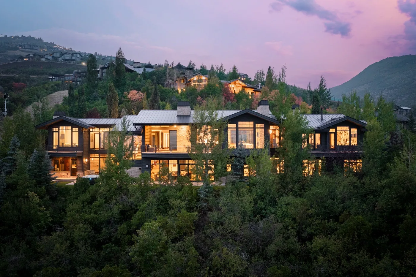 A row of warmly lit buildings sits among trees beneath a pink dusk sky.