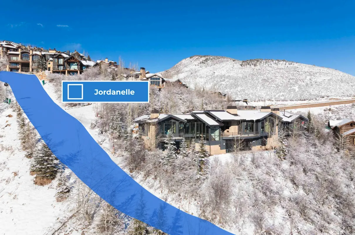 Aerial view of hillside homes beside a snow-covered slope under a clear sky.