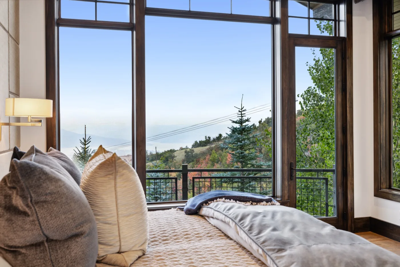 A bedroom with a bed beside large windows overlooking trees and hills.