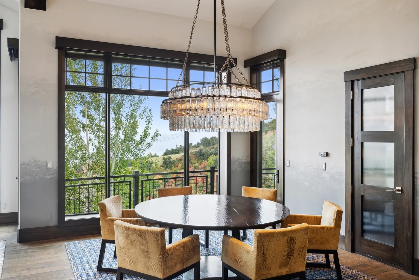 A dining area with a round table and large windows overlooking trees.