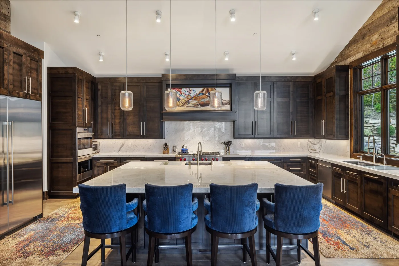 A spacious kitchen with dark cabinetry, a central island, and blue seating.