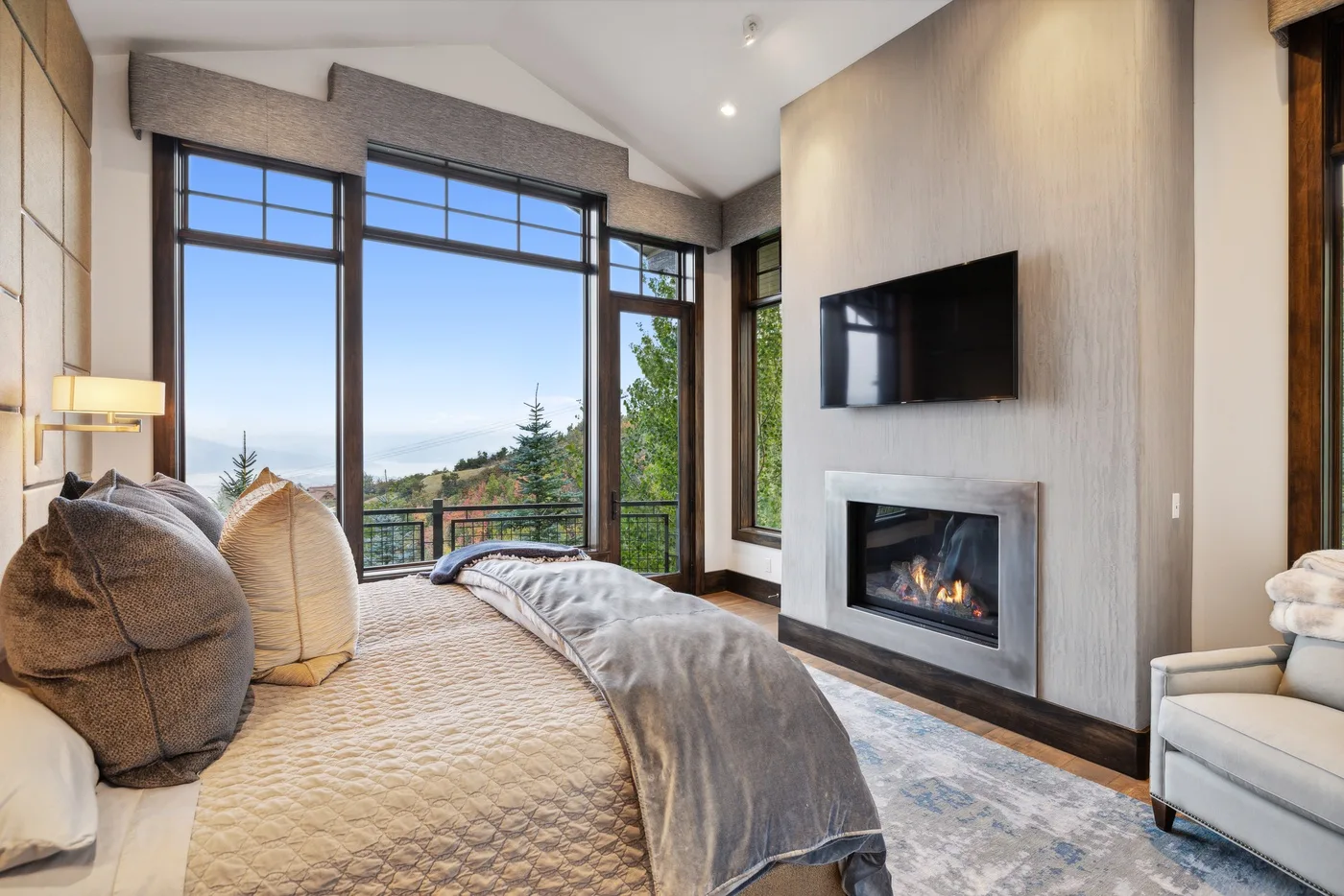 A bedroom with a large bed, floor-to-ceiling windows, and a fireplace.