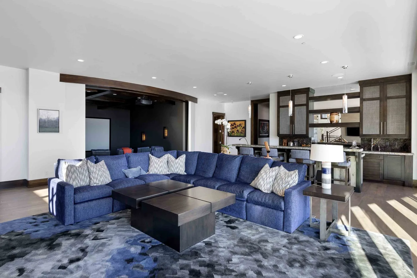 A spacious living room with blue seating and a coffee table opens onto a kitchen.