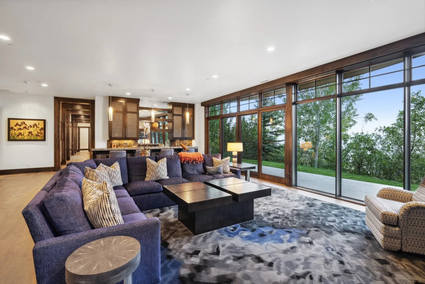 A spacious living room with sectional seating and large windows overlooking greenery.