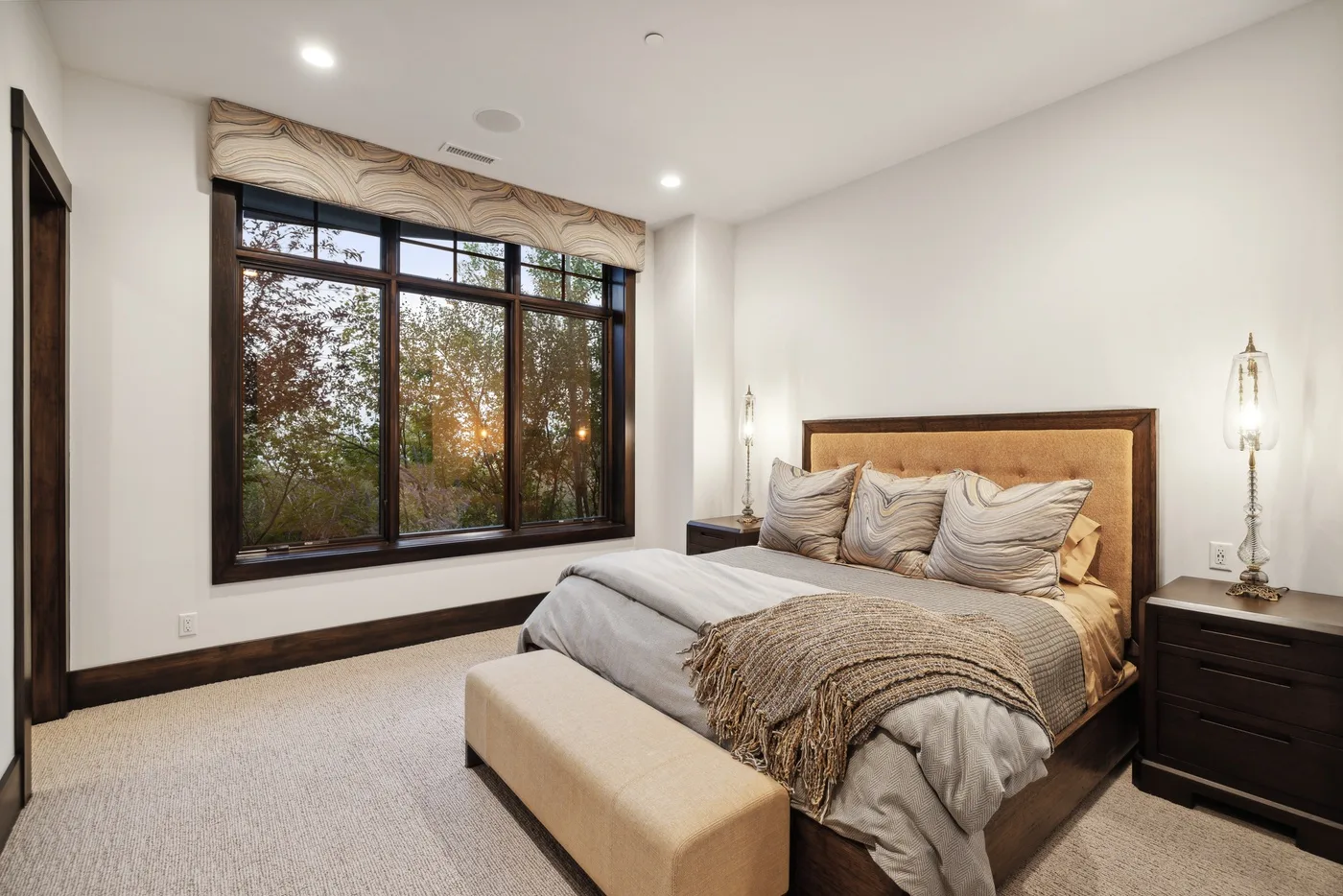 A bedroom with a bed beside a large window overlooking trees.