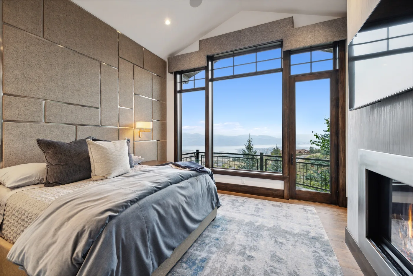 A bedroom with a bed beside large windows overlooking a distant landscape.