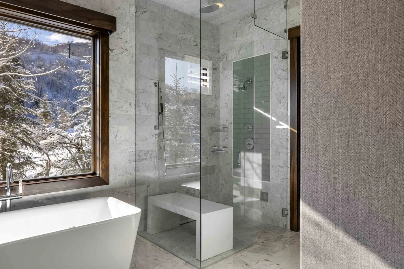 A bright bathroom with a freestanding bathtub beside a glass shower and a snowy view.