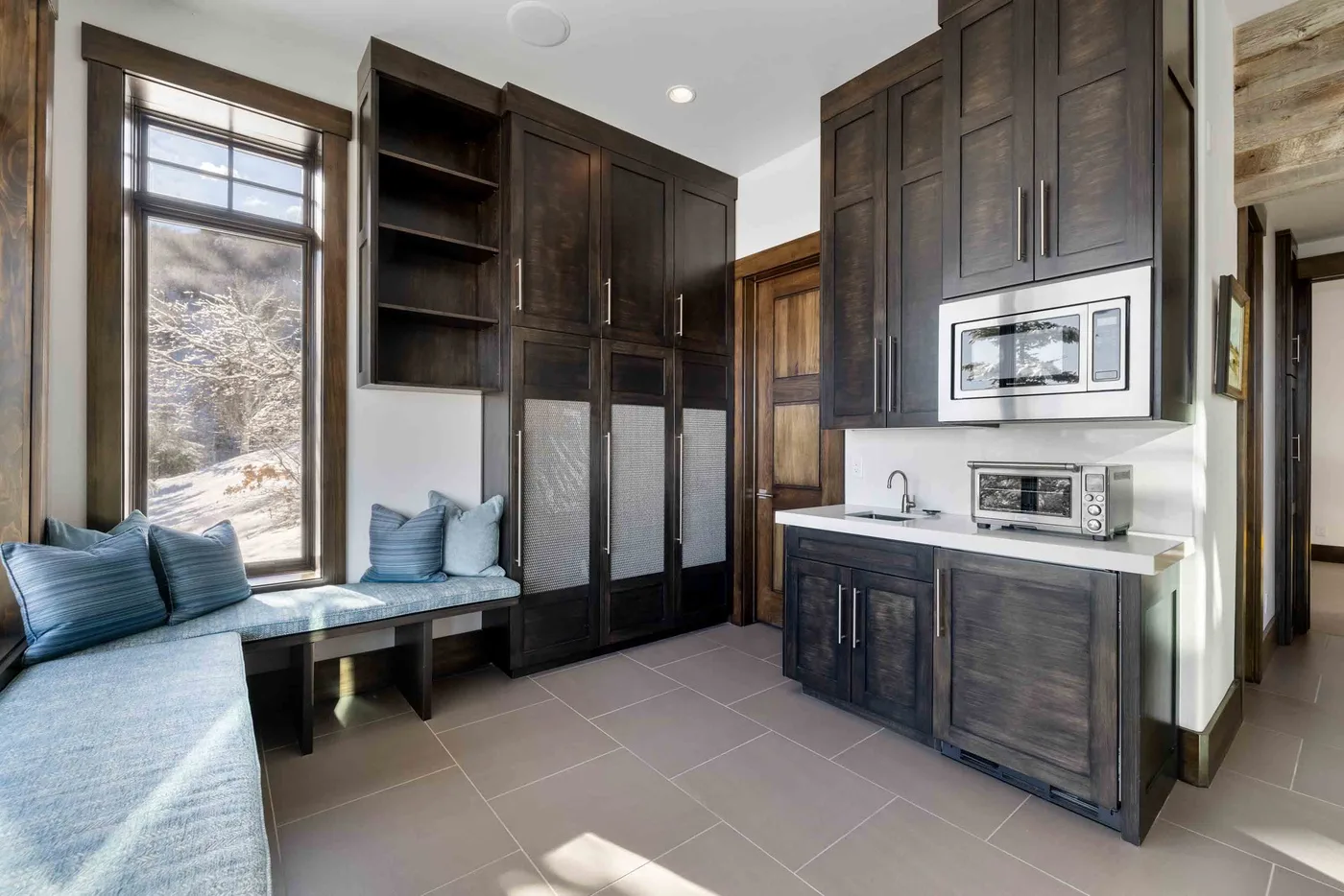 A room with dark built-in cabinets, a window seat, and a small kitchenette.