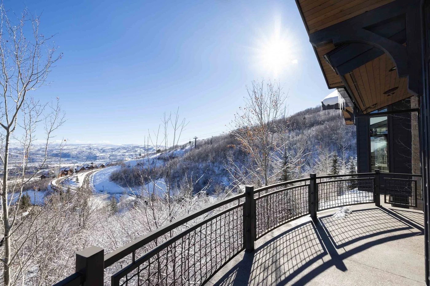A balcony overlooks a snowy valley, with a black metal railing in the foreground.