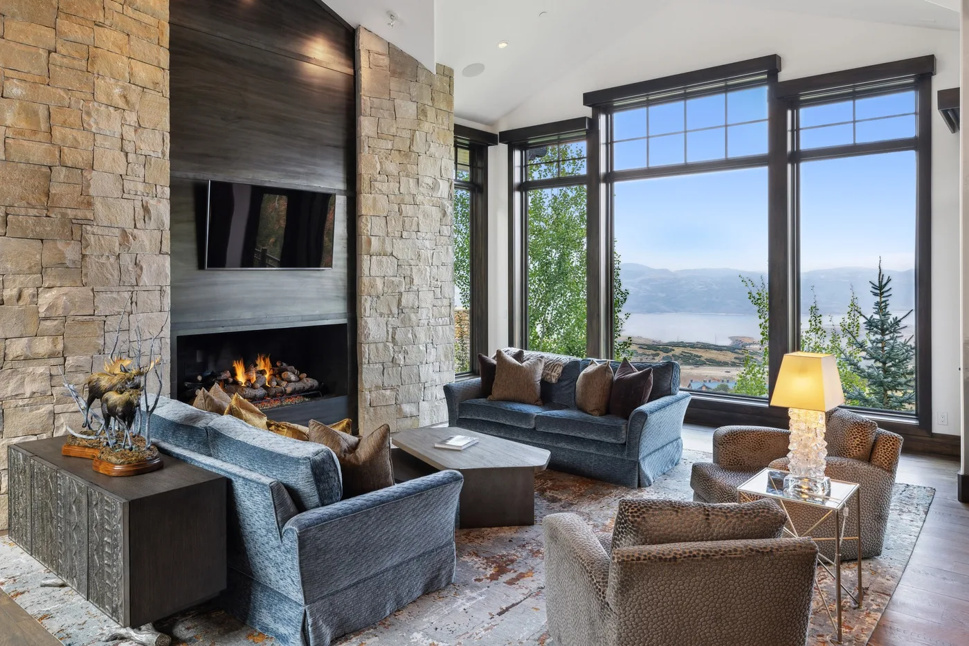 A living room with seating arranged around a fireplace and large windows.