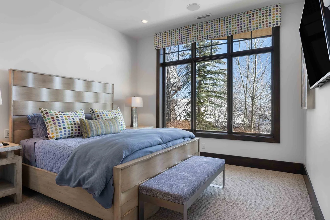 A bedroom with a bed beside a large window overlooking trees.