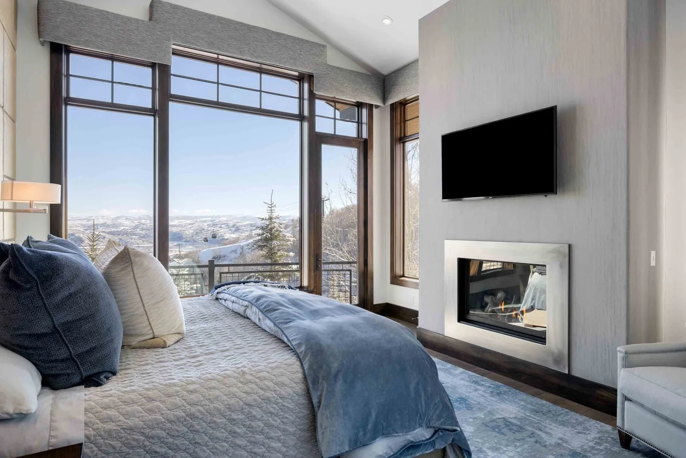 A bedroom with a bed beside large windows overlooking a snowy landscape.