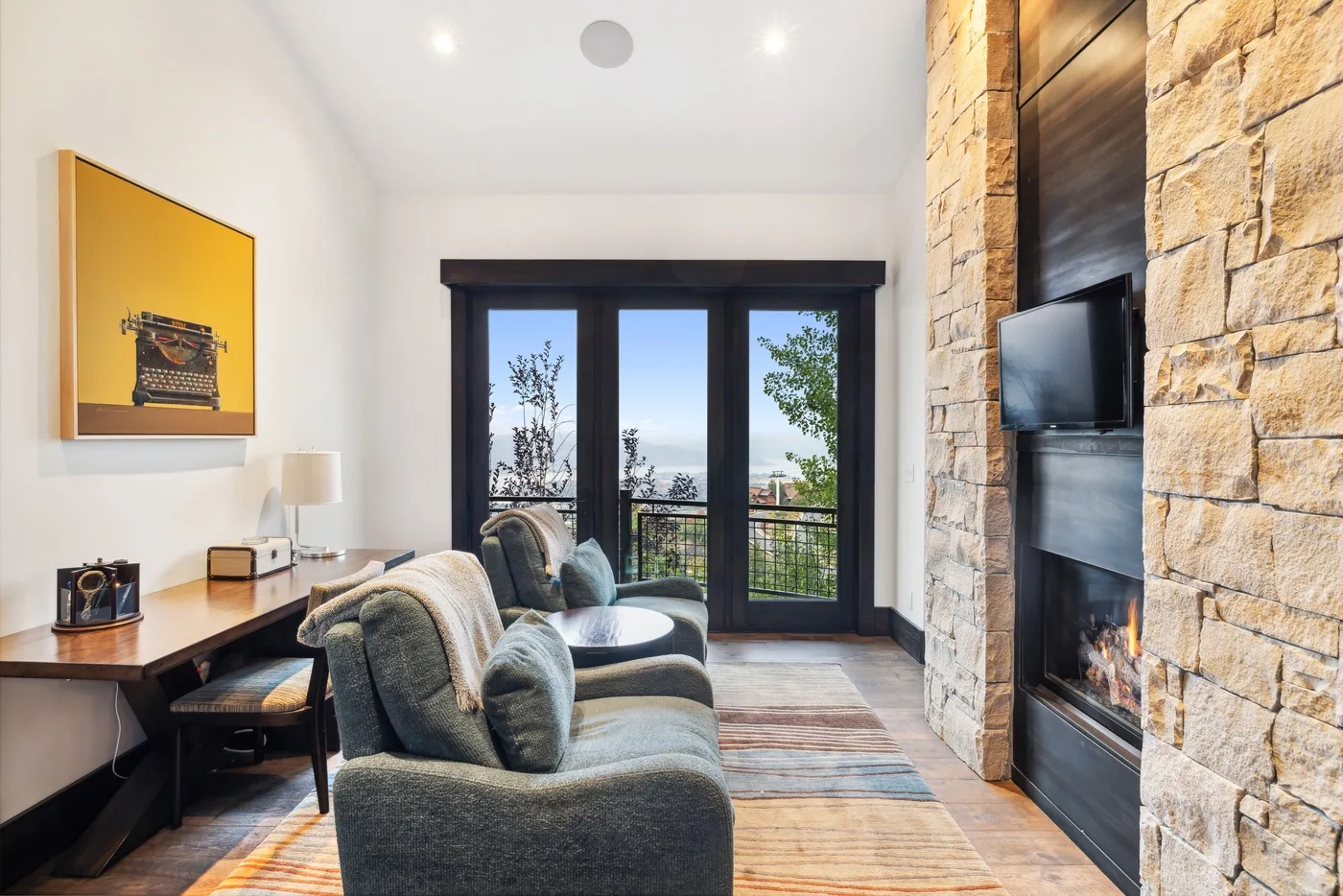 A living room with seating, a desk, and large glass doors opening onto a balcony.