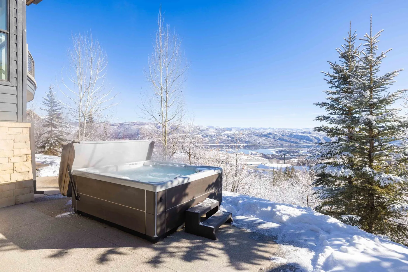 A hot tub sits on a snowy patio overlooking a winter landscape.