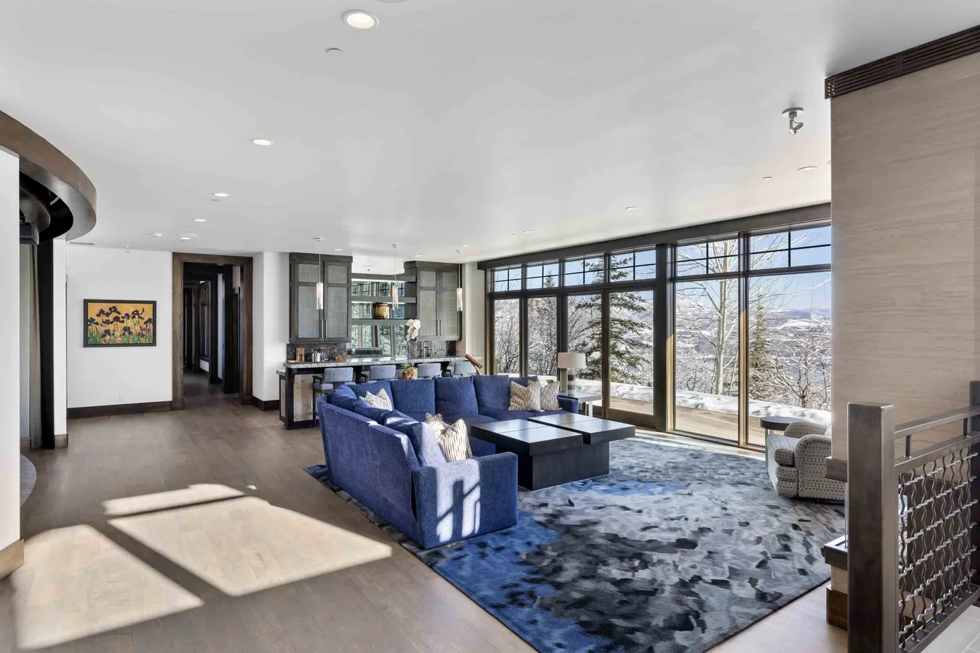A spacious living room with blue seating and large windows overlooking a snowy landscape.