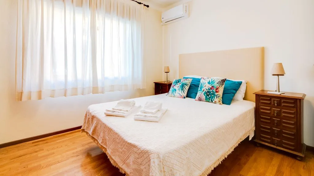 A bedroom with a neatly made bed and sheer curtains.