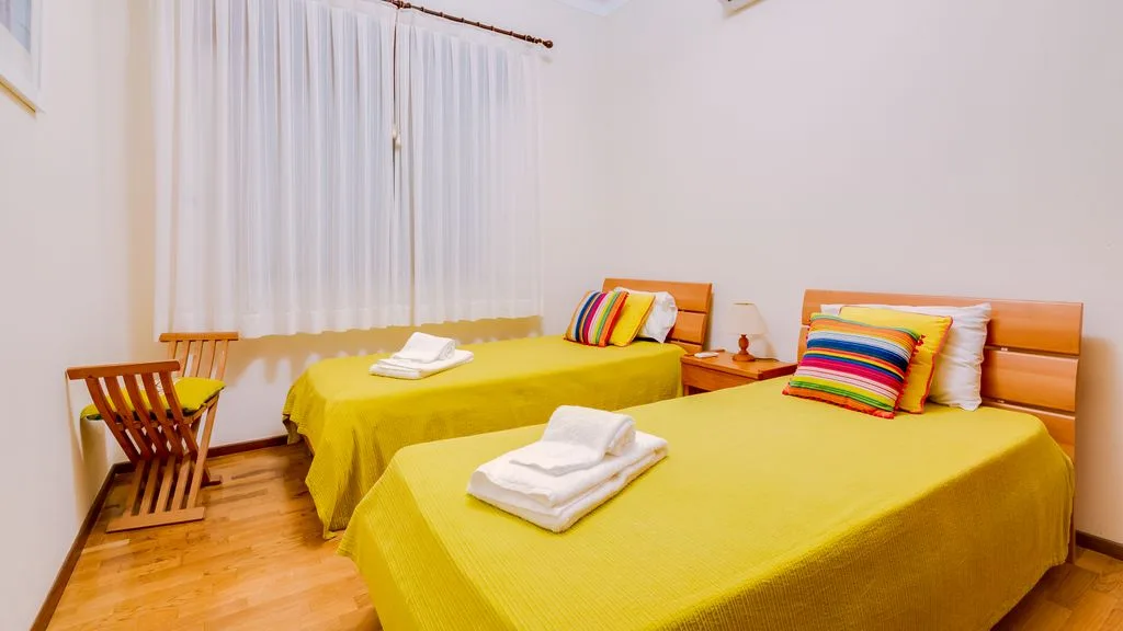 A bedroom with two beds covered in yellow bedspreads and white curtains.