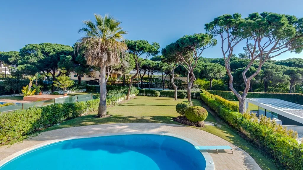 An outdoor swimming pool sits beside a landscaped garden with palm trees.