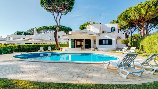 A modern white house stands beside a curved swimming pool and paved patio.